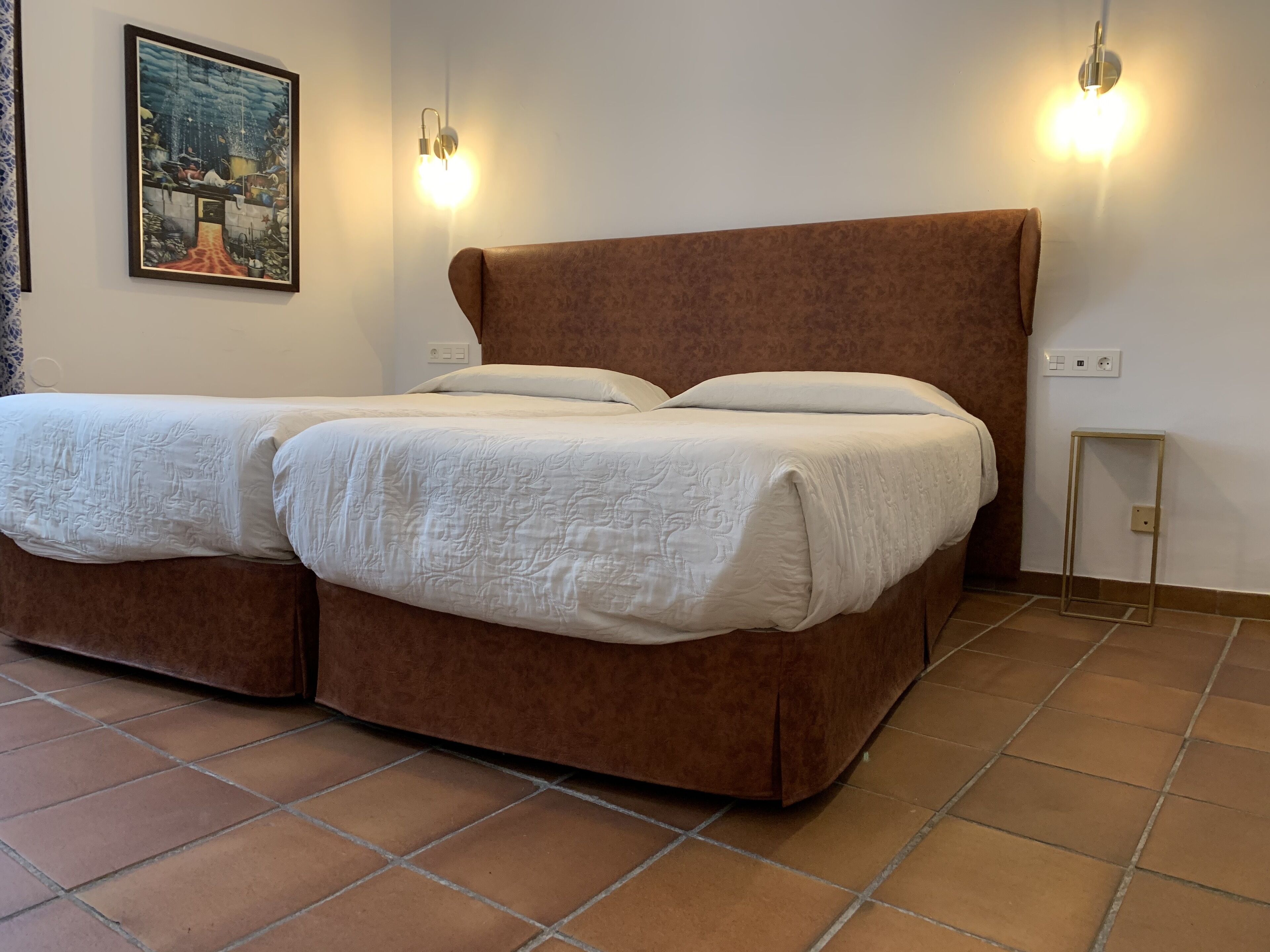 Una cama doble con cabecera marrón, dos mesitas de noche y un aplique de pared.