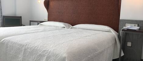 Cama doble con cabecera marrón, ropa de cama blanca y mesitas de noche con lámparas.