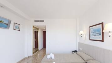 Habitación de hotel con cama, dos toallas enrolladas, lámpara de noche, teléfono y un cuadro en la pared.
