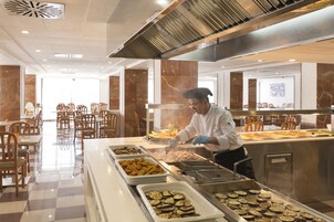 Zona de buffet con diferentes opciones de comida, un chef preparando alimentos y un área de estar con sillas y mesas.