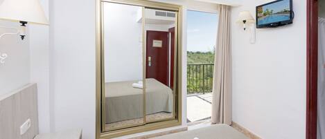 Ein Hotelzimmer mit Bett, Fernseher und einem Balkon mit Vorhängen, sowie einer Schiebetür zu einem weiteren Raum.