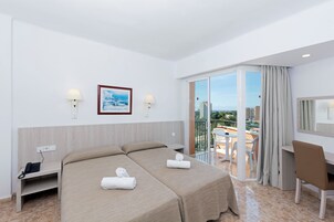 Habitación de hotel con dos camas, un escritorio, una silla y un balcón con vistas a la ciudad.