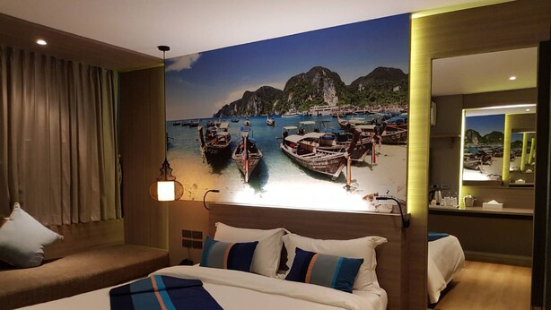 Quarto de hotel com cama, sofá, janela grande com vista para barcos e montanhas, e espelho na parede.