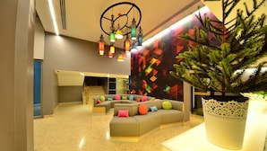 Um lobby moderno com um sofá curvo, uma grande planta em vaso e uma parede com padrão geométrico colorido.