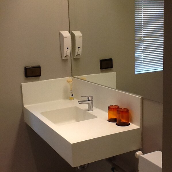 Un baño con un lavamanos blanco, un espejo y dos portavelas naranjas.
