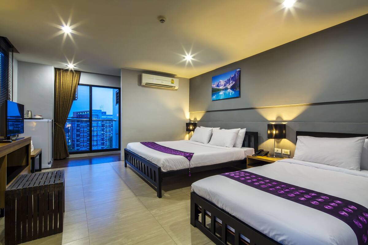 Habitación de hotel con dos camas, un escritorio, una silla, un televisor y ventana con vista a la ciudad.