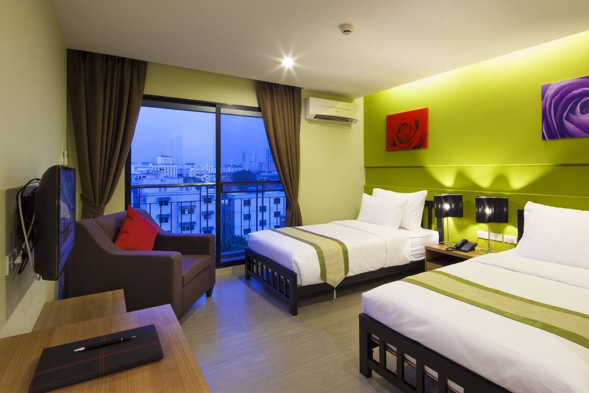 Habitación de hotel con dos camas, un sofá, un escritorio y vistas a la ciudad.
