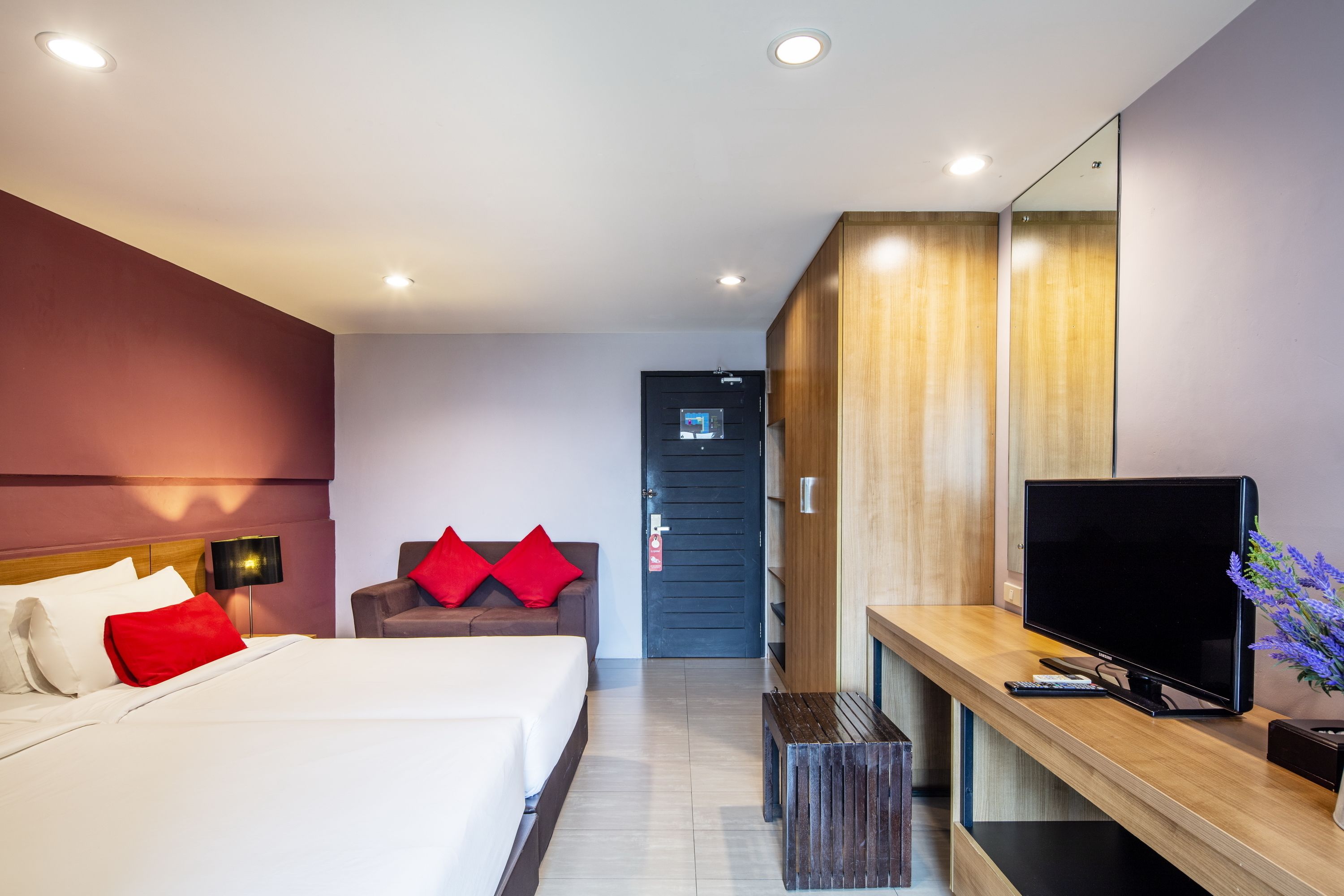 A modern hotel room with a large bed, a desk with a flat-screen TV, a mirror, and a door leading to another room.