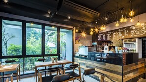 A modern cafe with wooden furniture, a counter with a menu, and large windows overlooking greenery.