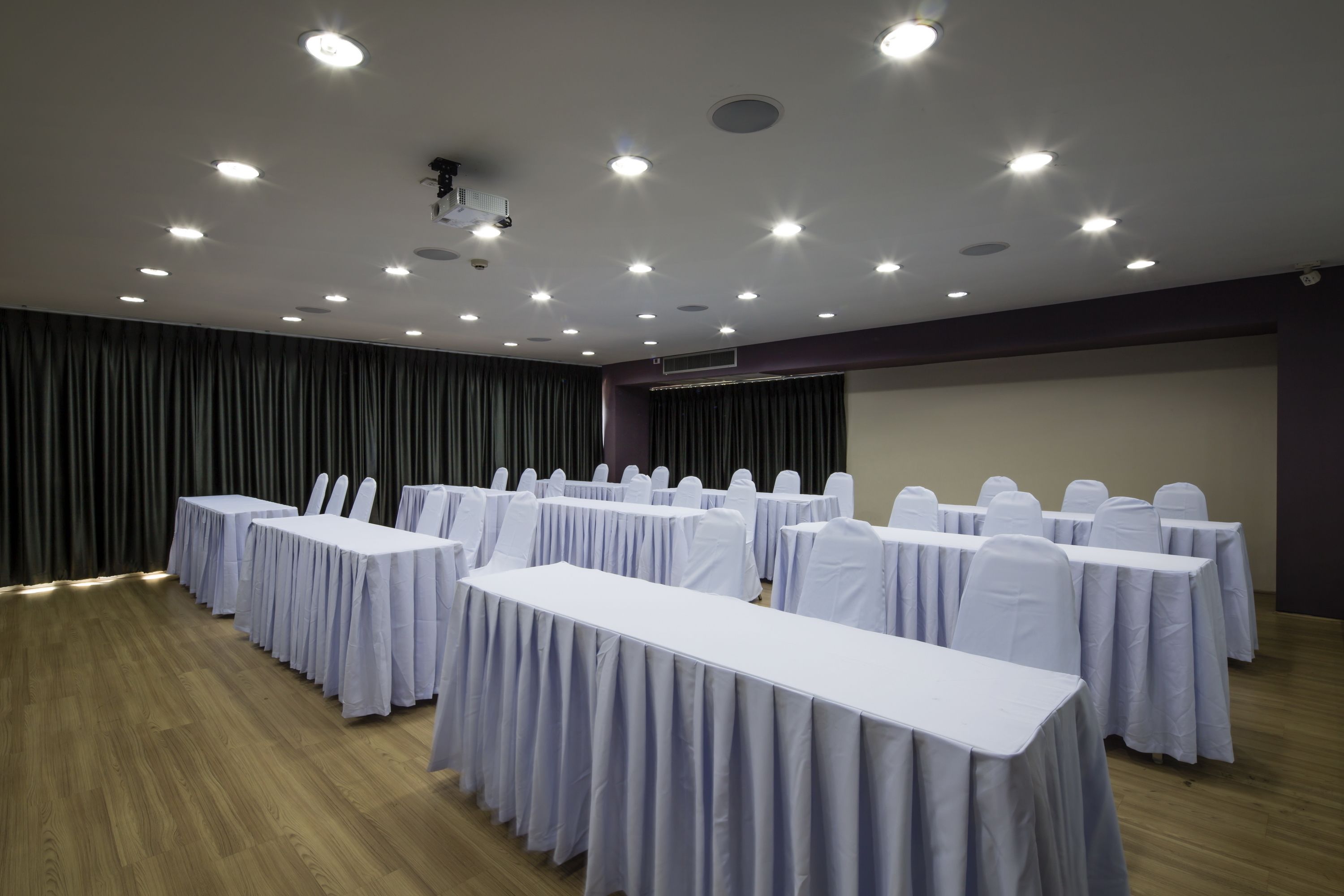 Ein Konferenzraum mit mehreren Tischen und Stühlen, ausgestattet mit Deckenleuchten und einem Projektor.