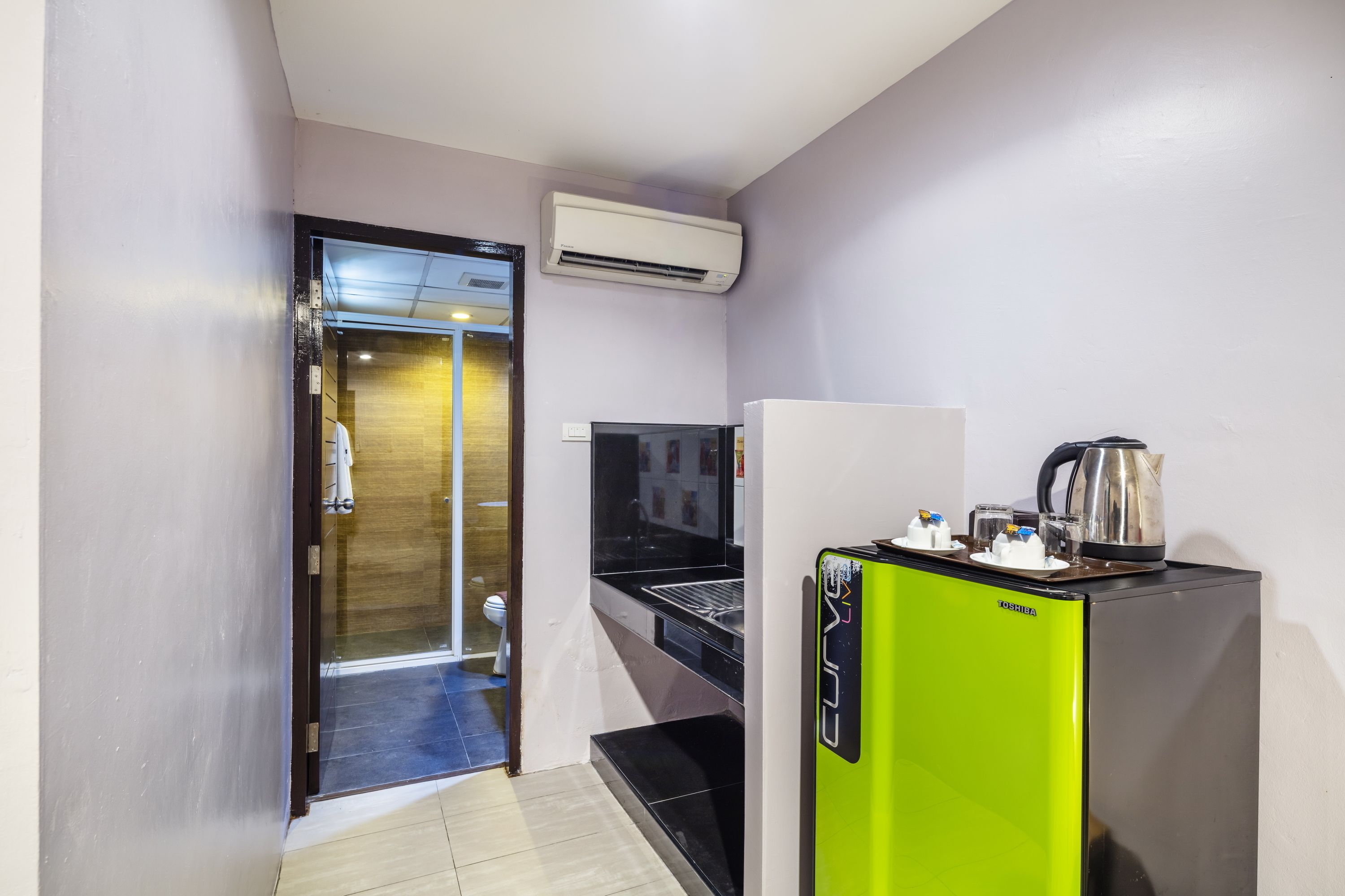 A compact kitchen with a green refrigerator, a microwave, and a kettle on top.