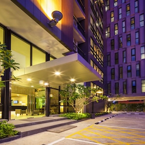 L’entrée d’un hôtel moderne, dotée d’une façade en verre, d’un espace extérieur aménagé pour s’asseoir et d’un parking.