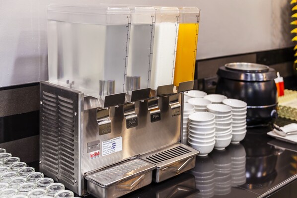 Un distributeur de boissons doté de plusieurs becs verseurs, une cafetière et des tasses empilées sur un comptoir.