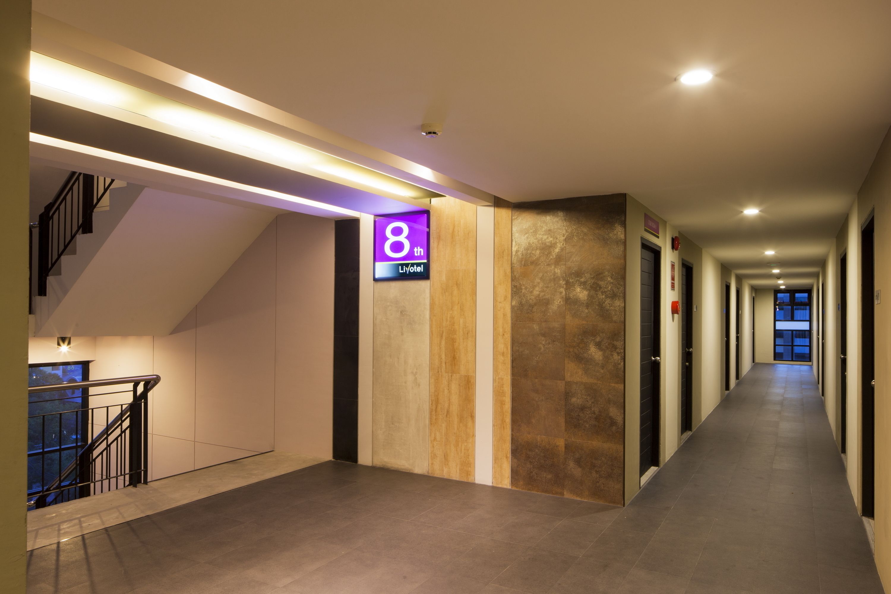 A modern hotel corridor with a staircase on the left, a sign indicating the 8th floor, and a long hallway with doors on both sides.
