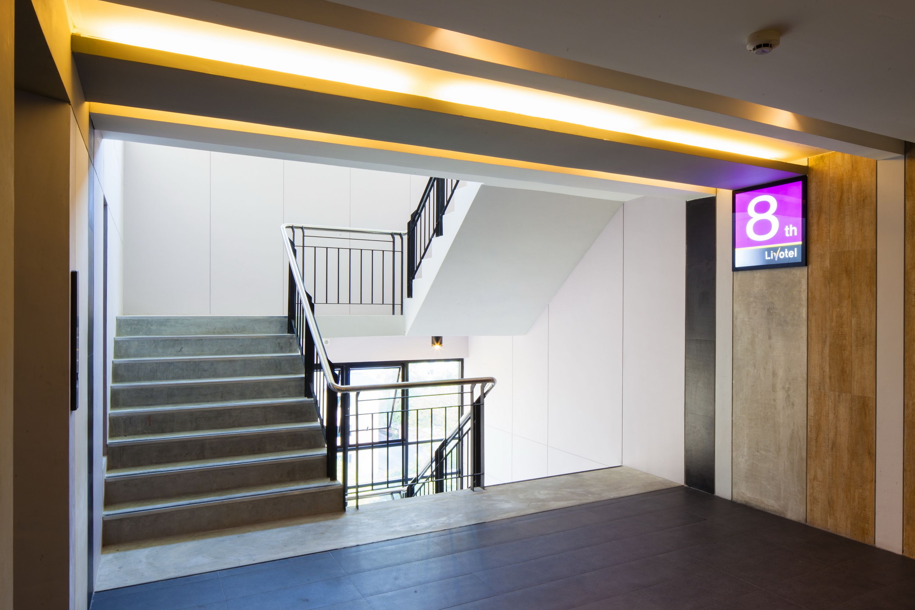 A modern hotel lobby with a staircase leading to an upper floor, a reception desk, and a sign indicating the 8th floor.