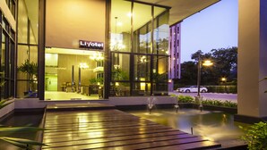A modern hotel entrance with glass doors, a reception area, and a water feature in front.