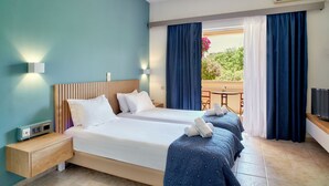 A hotel room with two beds, a wooden headboard, a nightstand with a power outlet, a TV, and a balcony with a table and chairs.