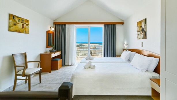 A hotel room with a large bed, a desk, a chair, and a view of the sea.