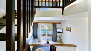 A modern interior with a staircase, a dining area with a table and chairs, a TV, and a view of a pool and outdoor seating.