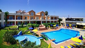 A hotel with a swimming pool, sun loungers, and a garden area.