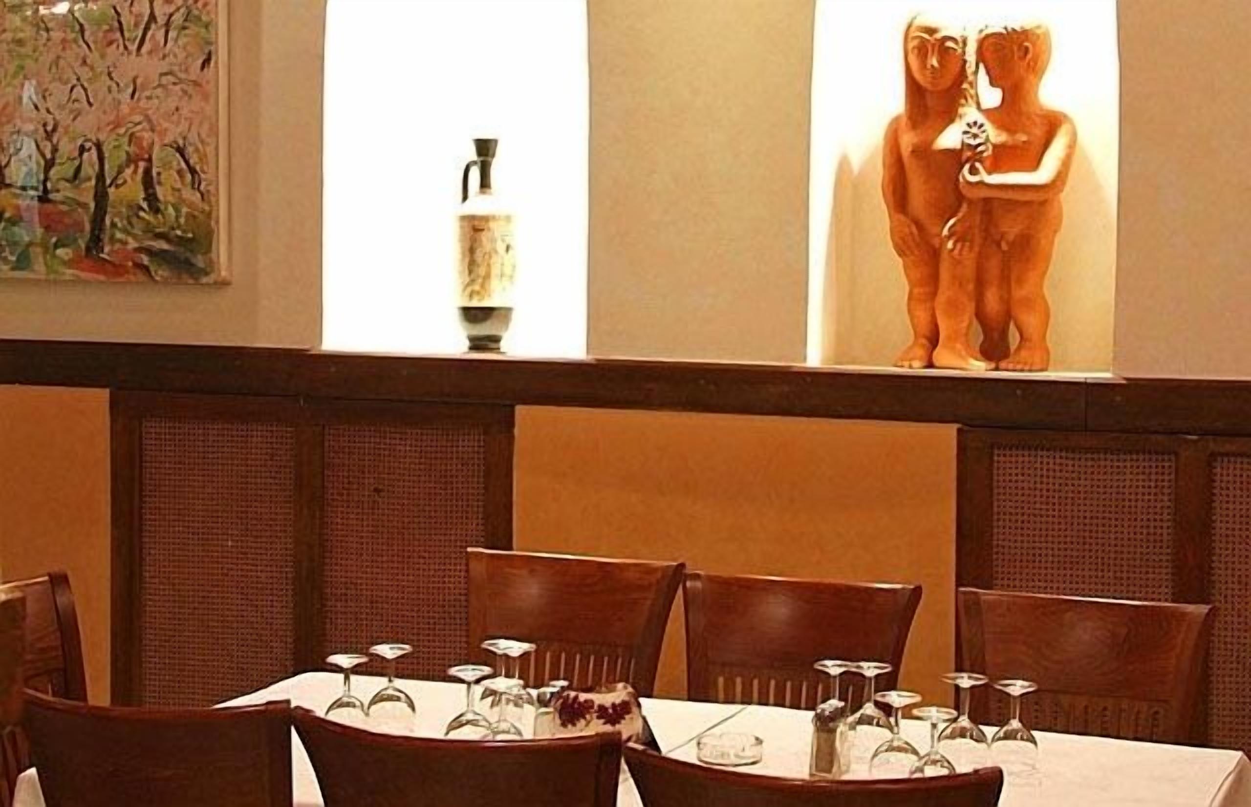 A dining area with tables set for four, wooden chairs, and a painting on the wall.