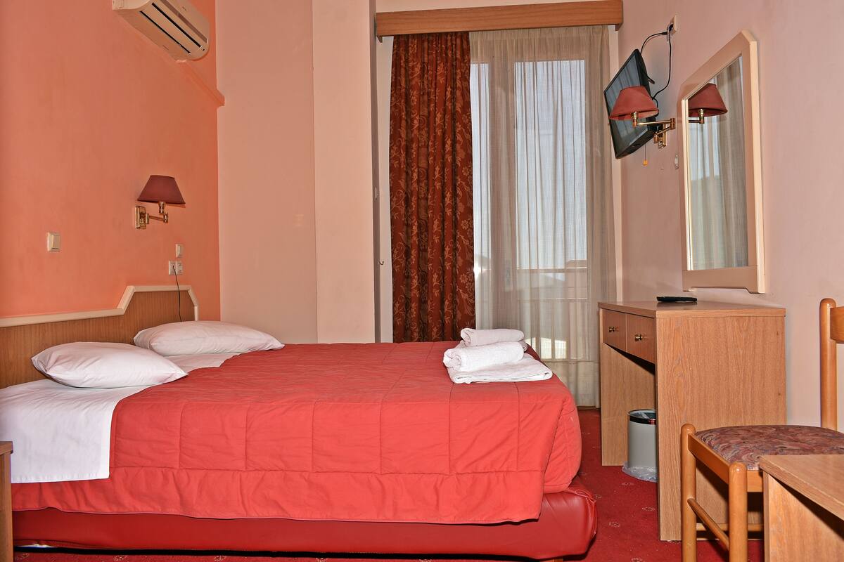 A hotel room with a bed, a desk, a chair, a mirror, and a window with curtains.