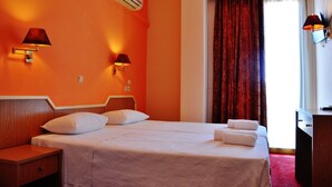 A hotel room with a double bed, two bedside lamps, an air conditioner, a wooden nightstand, a desk, and a red curtain. - Iniohos Hotel Restaurant (Delphi)