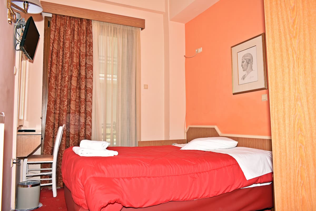 A hotel room with a bed, a desk, a chair, a television, and a window with curtains.