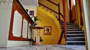 A staircase with a wooden handrail and marble steps, leading to a landing with a potted plant and a framed picture. - Iniohos Hotel Restaurant (Delphi)