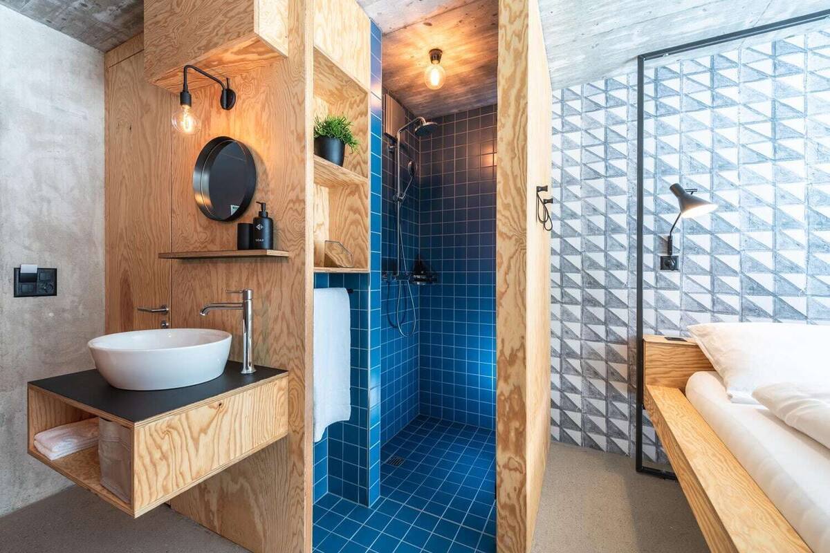 A modern bathroom with a wooden vanity, a large sink, and a shower with blue tiles.