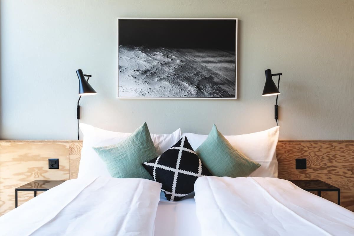 A neatly made bed with white bedding and patterned pillows, a framed artwork above, and two bedside lamps on wooden nightstands.
