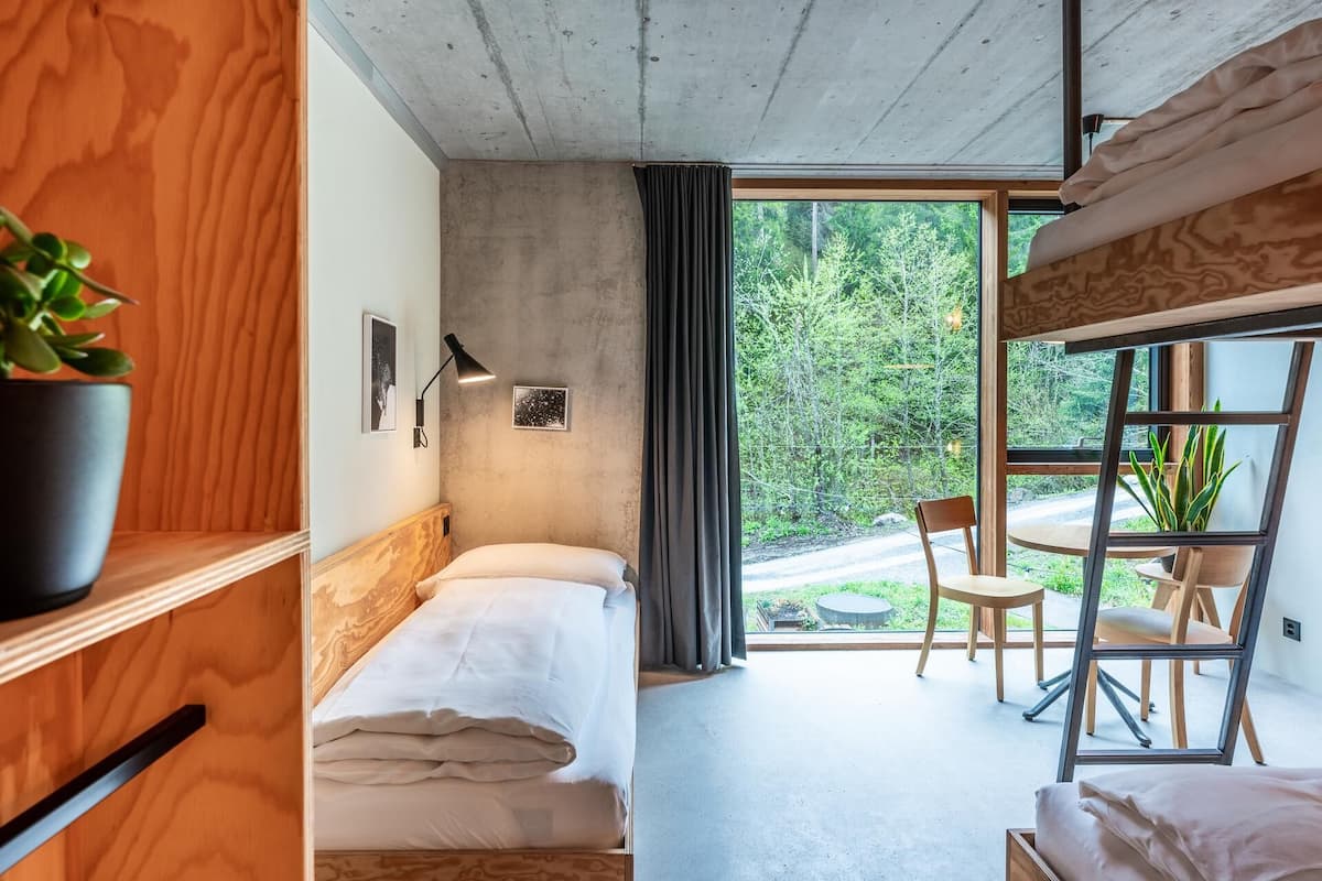 A modern bedroom with a large window, a wooden headboard, a bedside table, and a potted plant.