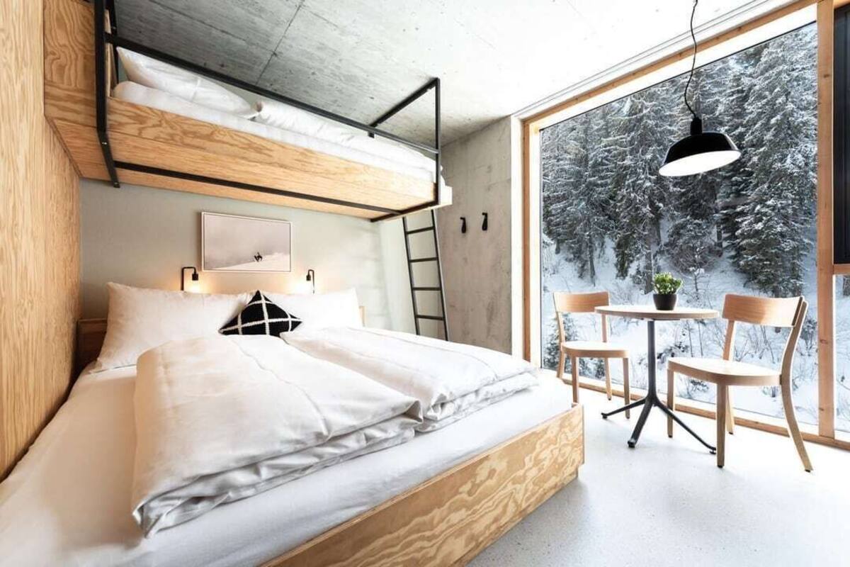 A modern bedroom with a bunk bed, a desk, and chairs near a large window with a snowy view.