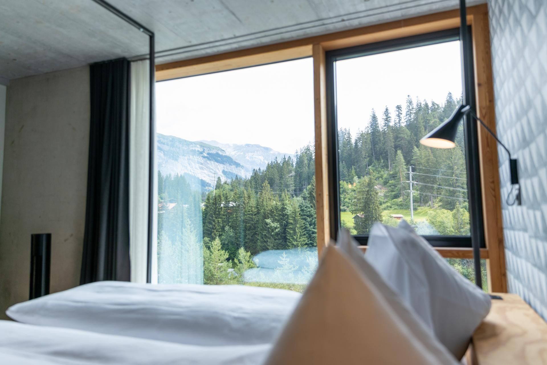 Een slaapkamer met een groot raam dat uitzicht geeft op een bos en bergen.