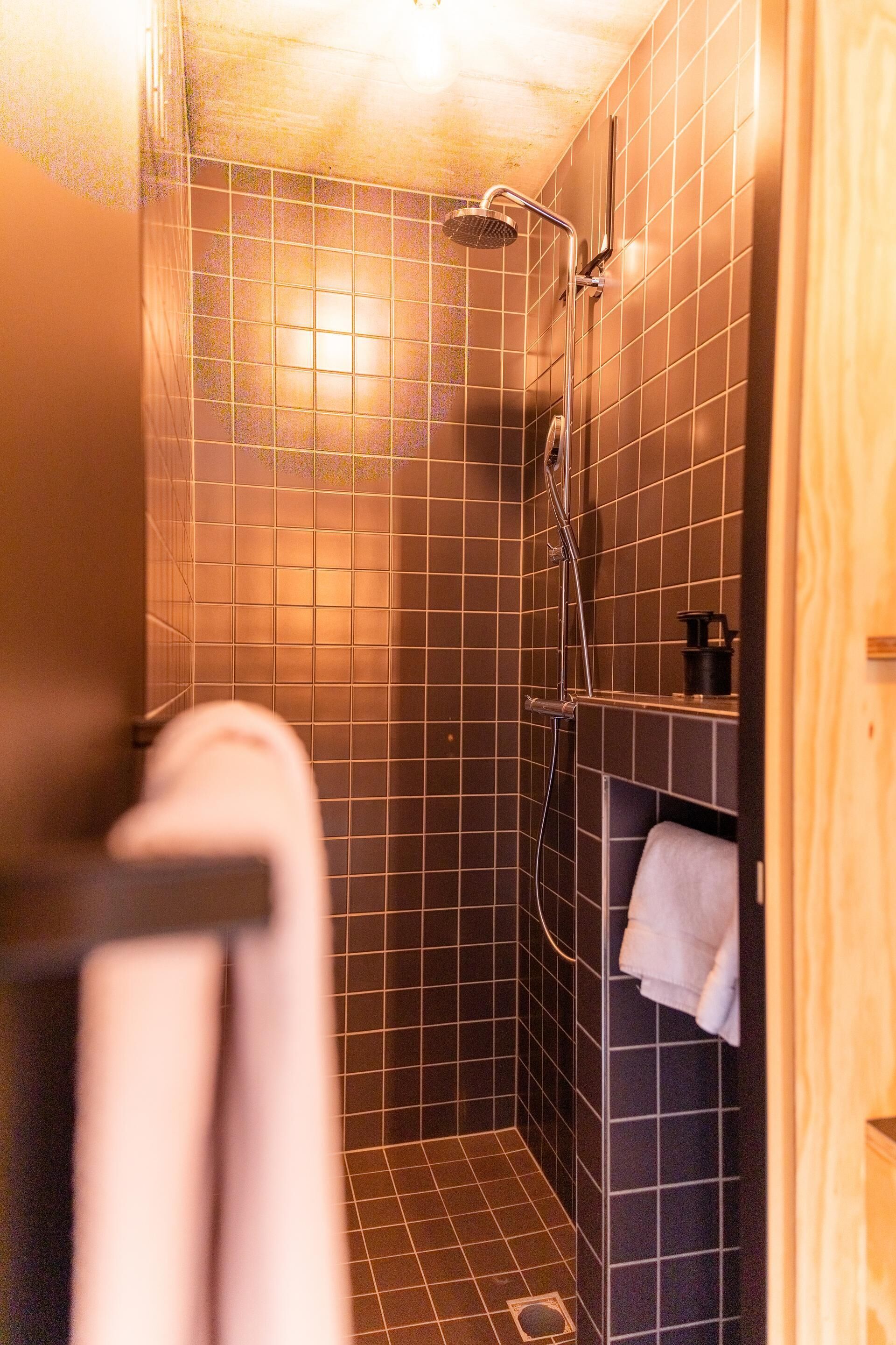 A small, tiled shower area with a handheld showerhead and a towel rack.