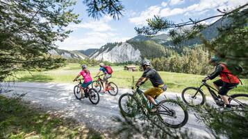 Un grupo de ciclistas en un camino pavimentado, rodeado de vegetación y montañas.
