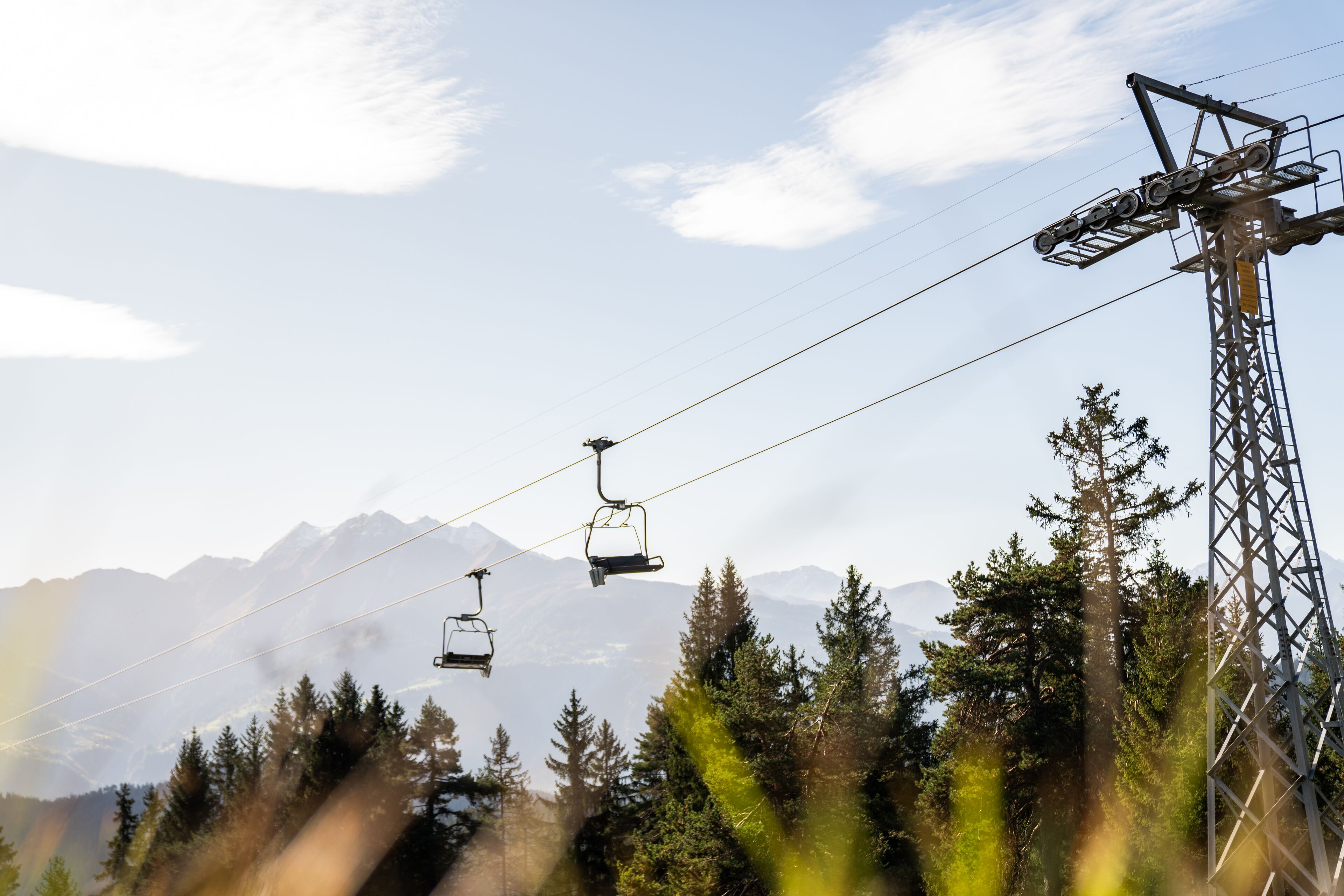 A ski lift with cables and chairs against a mountainous backdrop.