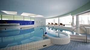 Una piscina interior con agua azul cristalina, un jacuzzi y sillones de descanso junto a la ventana.
