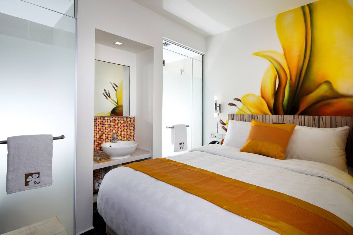 A hotel room with a large bed, a bathroom with a sink and mirror, and a vibrant flower painting on the wall.