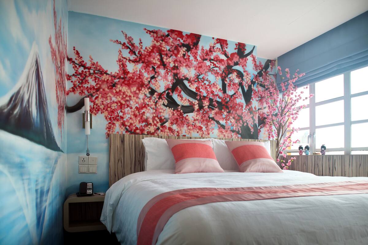 A hotel room with a large bed, a nightstand, a wall-mounted telephone, and a window with curtains.