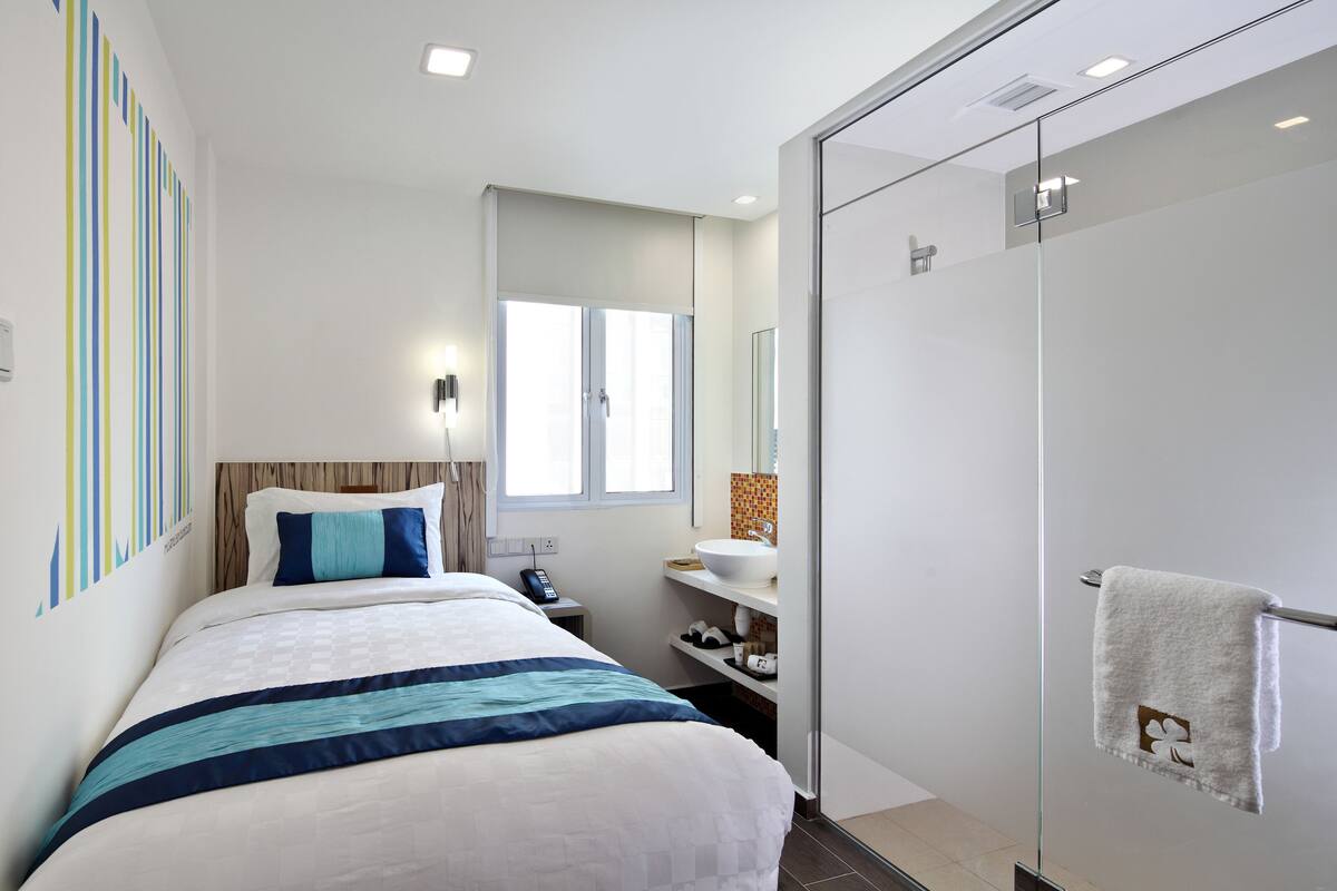 A modern hotel room with a bed, bedside table, and a glass-enclosed shower.
