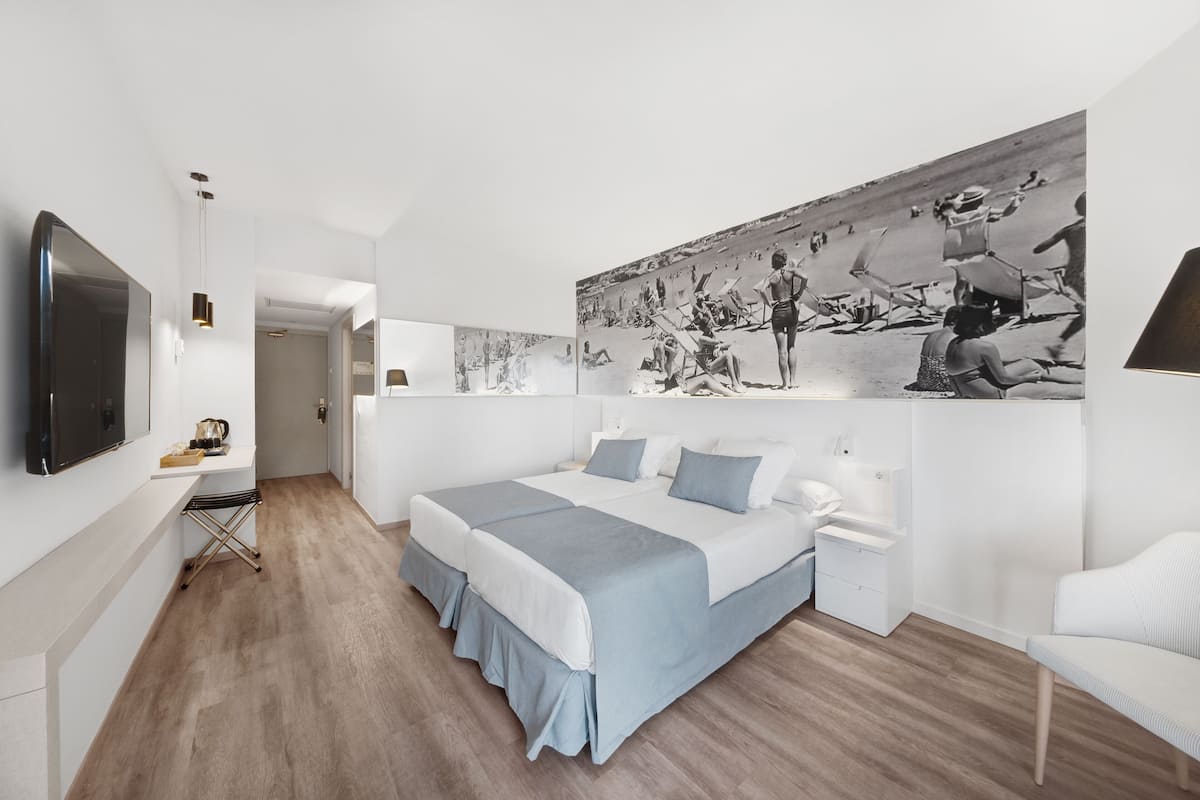 Une chambre d’hôtel moderne avec un grand lit, un téléviseur à écran plat, un bureau et une grande photographie en noir et blanc accrochée au mur.