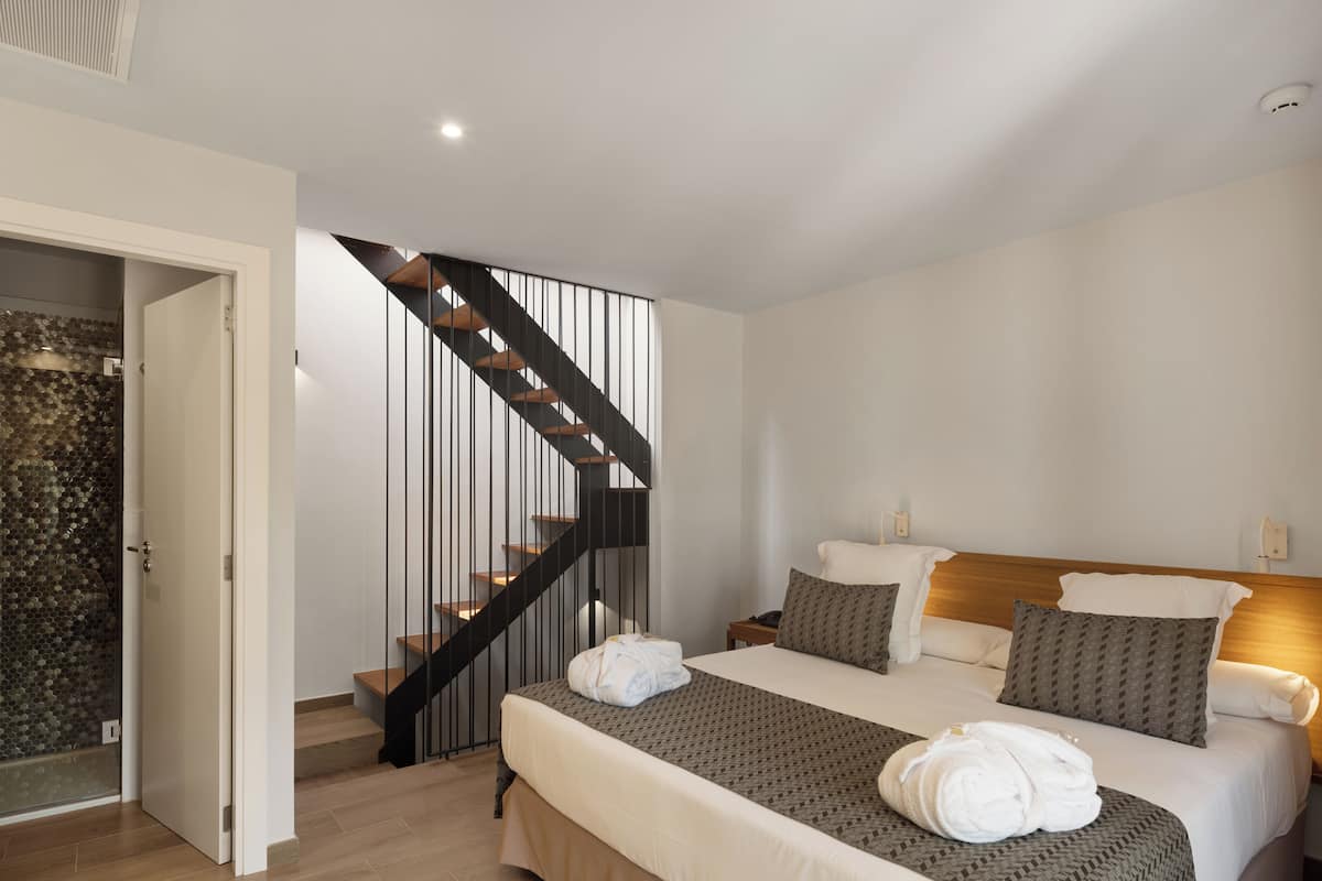 Une chambre d’hôtel avec un lit, une tête de lit en bois, une table de chevet et un escalier moderne.