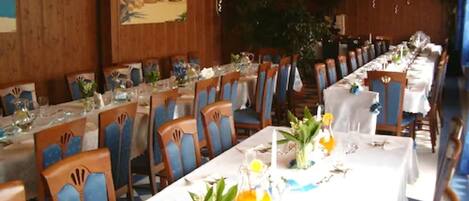 A dining area with long tables set for service, wooden paneling on the walls, and a large painting of a beach scene.