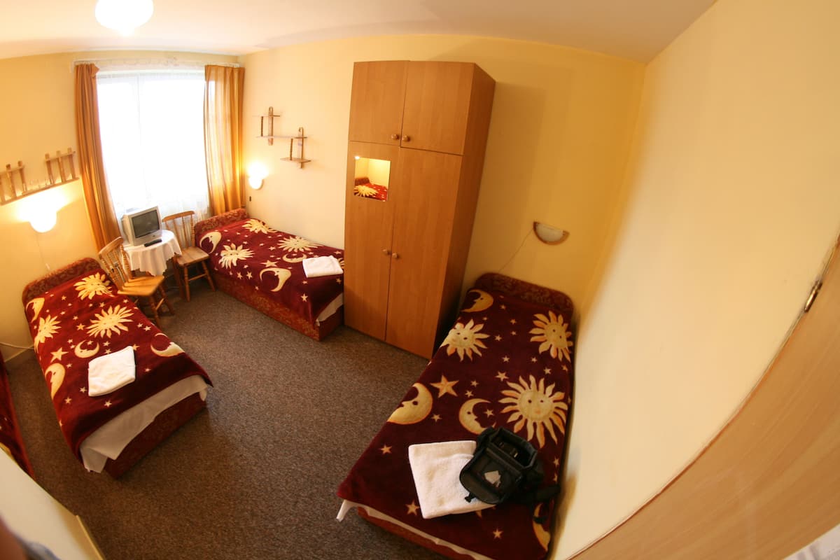 A hotel room with two beds, a desk with a computer, a wardrobe, and a window with curtains.