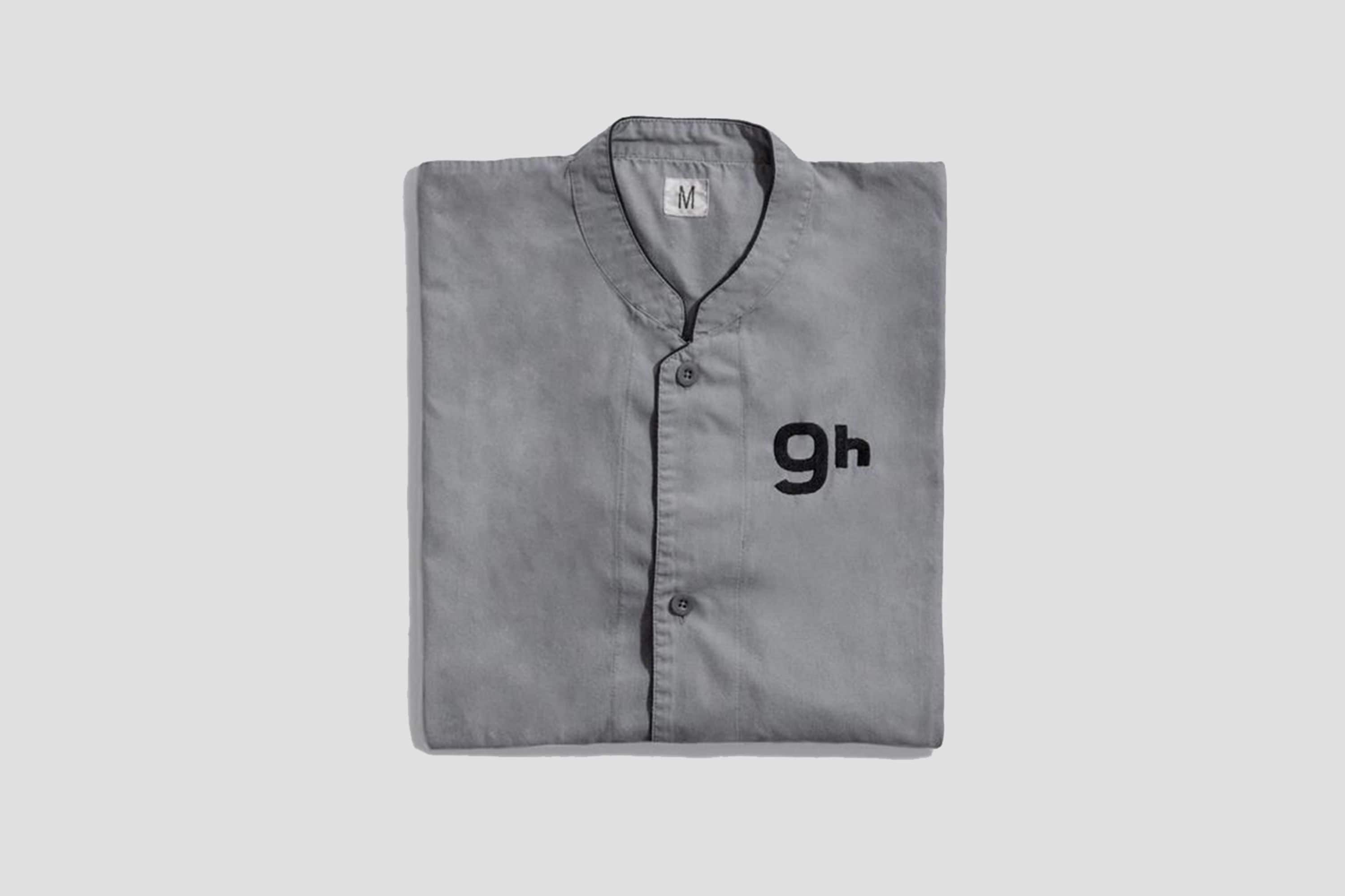 A folded grey shirt with a collar and buttons, featuring the letters "gh" on the front.