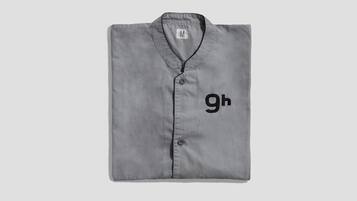 A folded grey shirt with a collar and buttons, featuring the letters "gh" on the front.