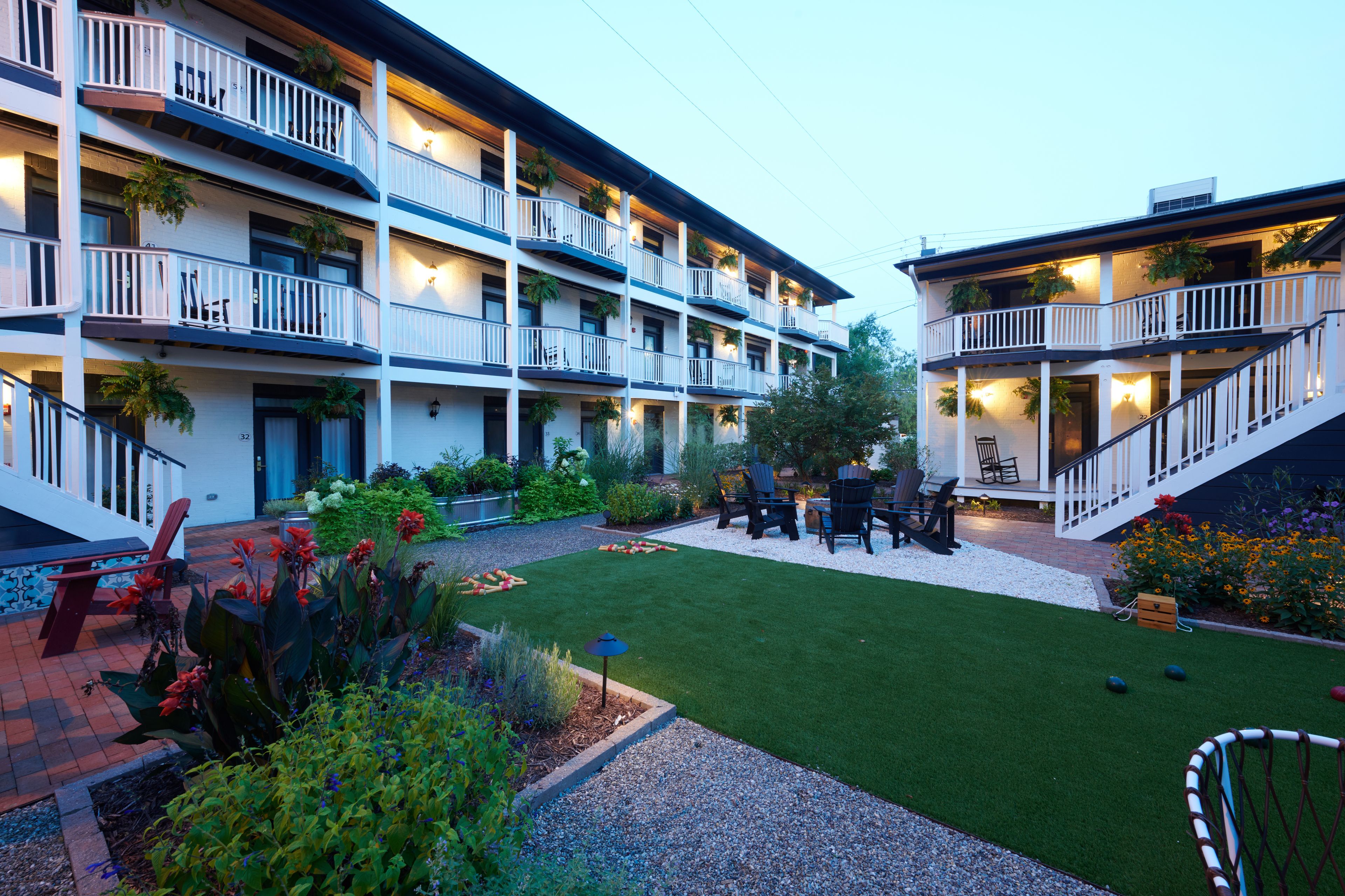 Un hotel de varios pisos con balcones, mobiliario exterior y un jardín bien cuidado.