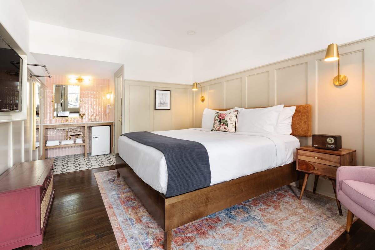 A hotel room with a large bed, bedside table, and a small desk with a chair.
