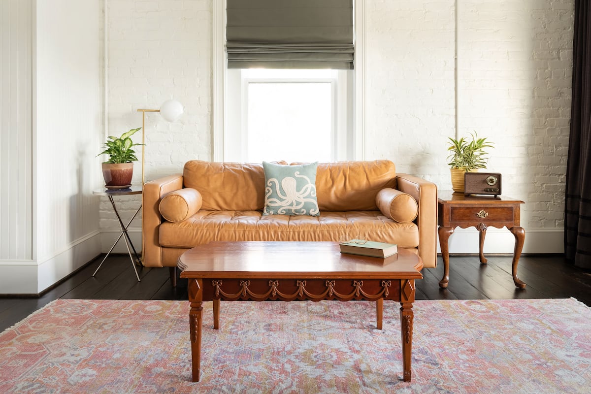 A living room with a leather sofa, a wooden coffee table, a patterned rug, a small side table with a lamp, and a radio.